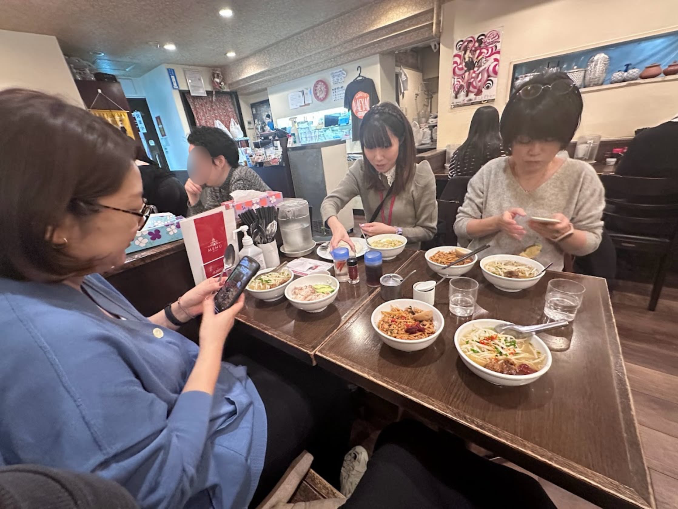 タイ料理屋で出てきた食事を3人がスマホカメラで撮影している写真